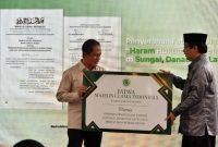 Wasekjen MUI Bidang Ekonomi dan Lingkungan Hidup Hazuarli Halim (kanan) menyerahkan secara simbolis fatwa MUI tentang haram hukumnya membuang sampah di sungai, danau dan laut kepada Menteri Lingkungan Hidup Hanif Faisol Nurofiq (kiri) saat peluncuran di Komunitas Iklim Sungai Cikeas (KISUCI), Babakan Madang, Bogor, Jawa Barat, Minggu (15/2/2026).(Foto: Tera Nusantara.com)